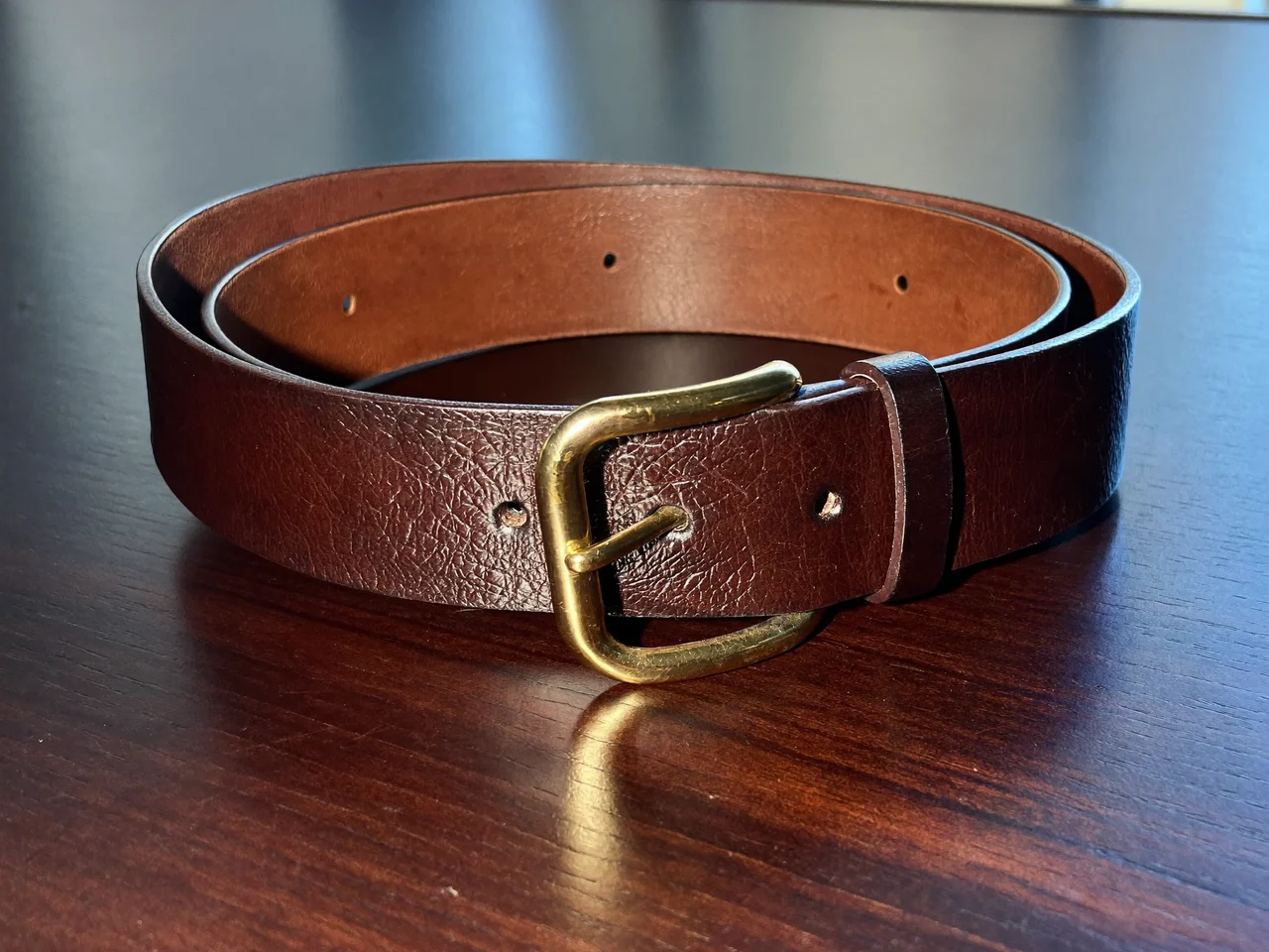 Cintura classica in pelle marrone con fibbia in ottone su tavolo scuro