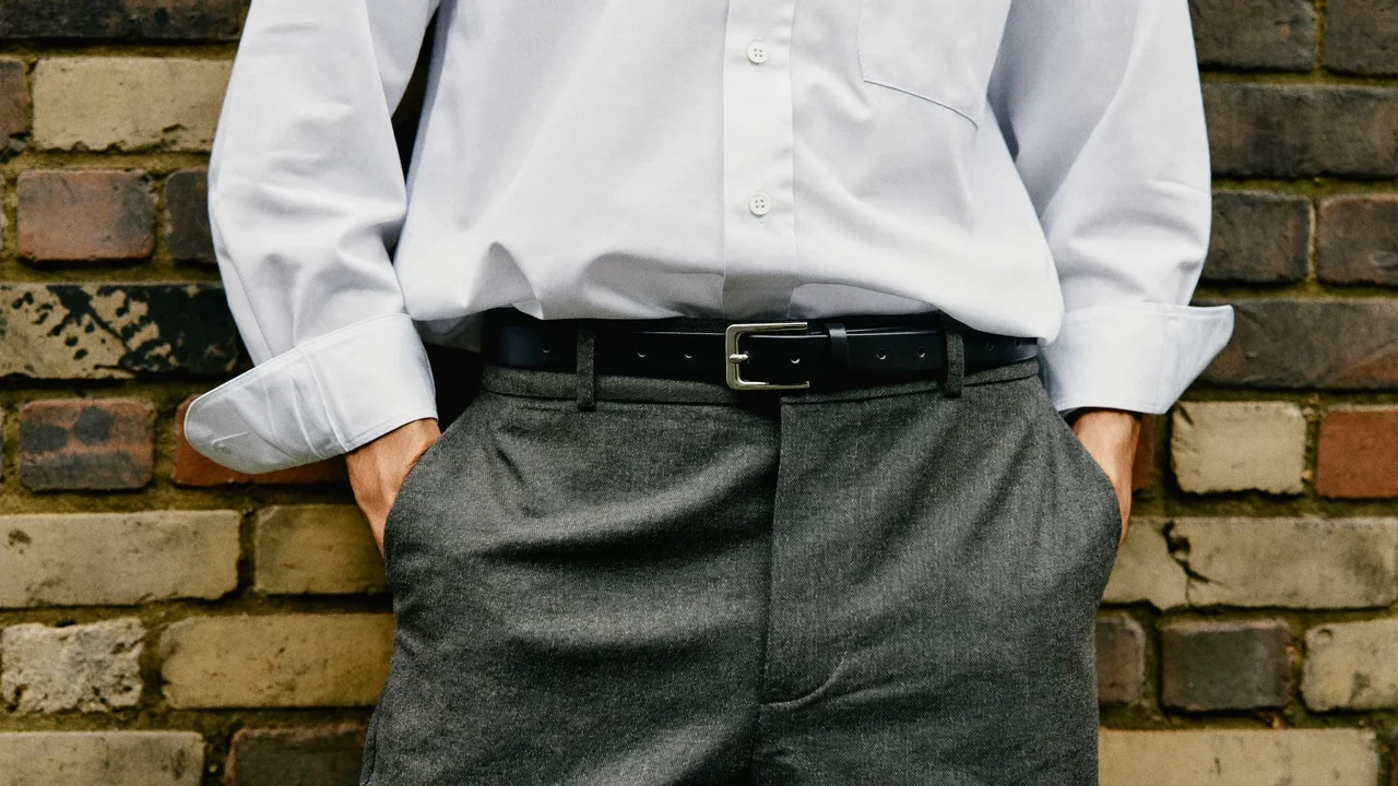 Vita con pantaloni sartoriali e camicia bianca, cintura in pelle su muro di mattoni